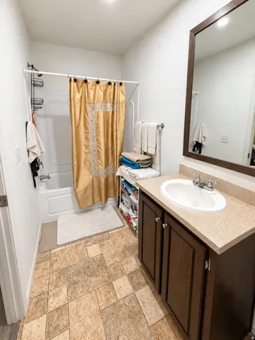 Bathroom featuring a white tub with shower, wood-finish vanity with countertop and integrated sink, and patterned floor tiling