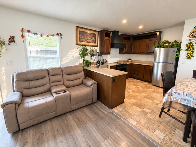 Open-concept living space featuring wood-finish flooring, a kitchen with dark wood cabinetry, a stainless steel refrigerator, and recessed lighting