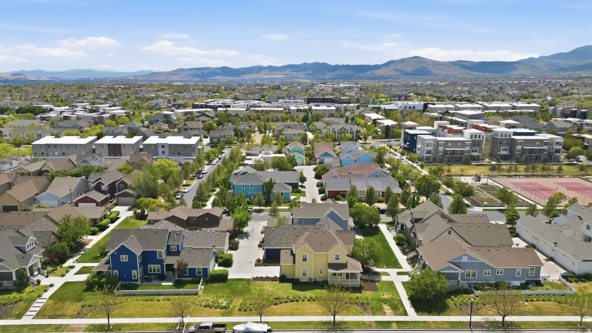 Residential neighborhood featuring single-family homes and multi-story buildings, mature trees, and mountainous backdrop