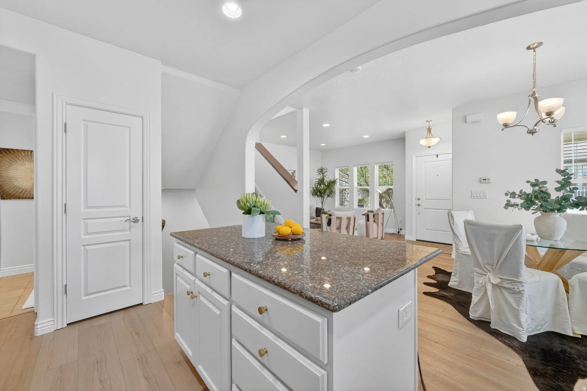 Kitchen island with a speckled countertop, white cabinetry with brass-finish hardware, and wood-finish flooring