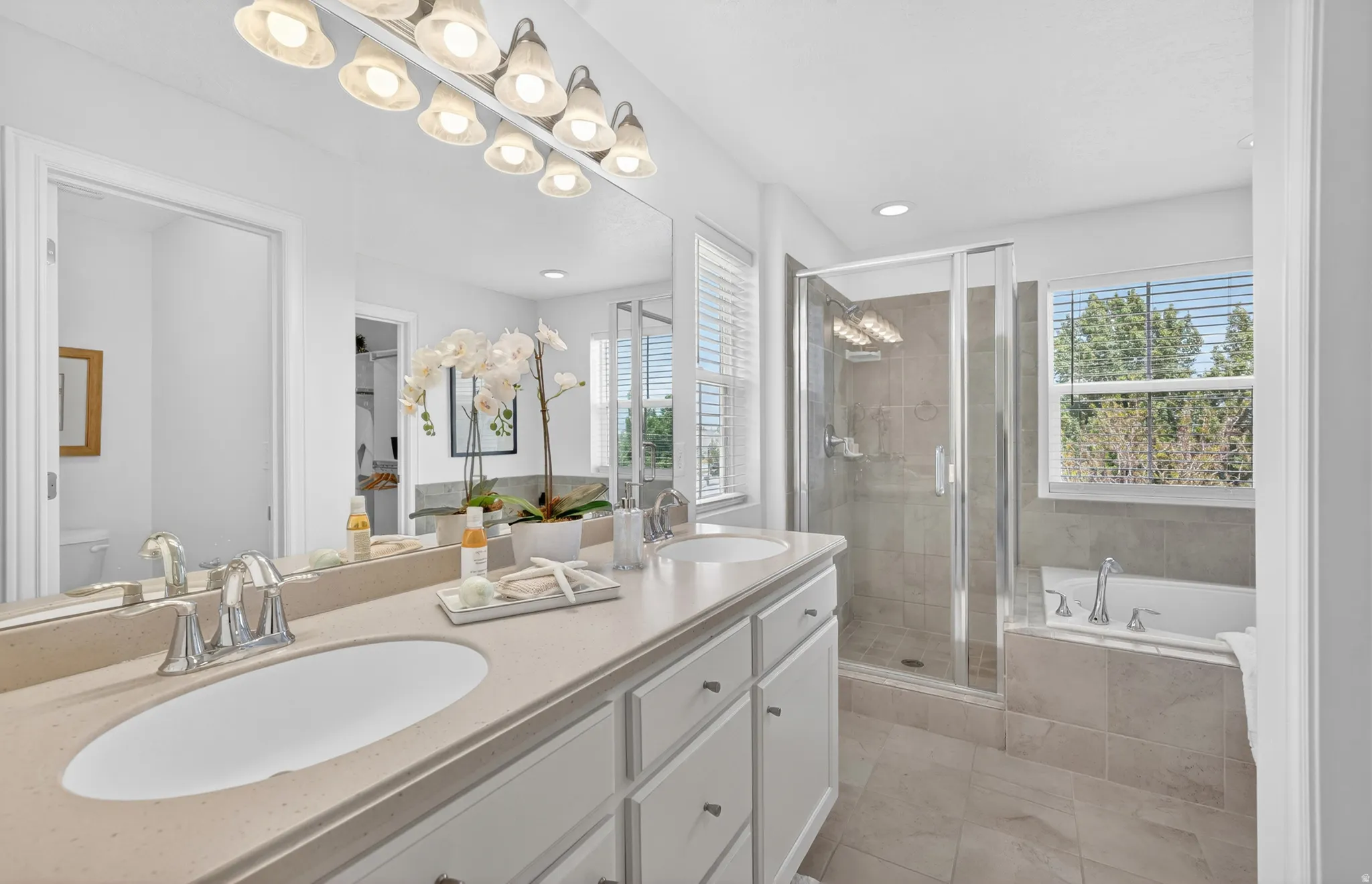 Dual vanity with integrated sinks, recessed lighting, glass-enclosed shower, and a built-in soaking tub