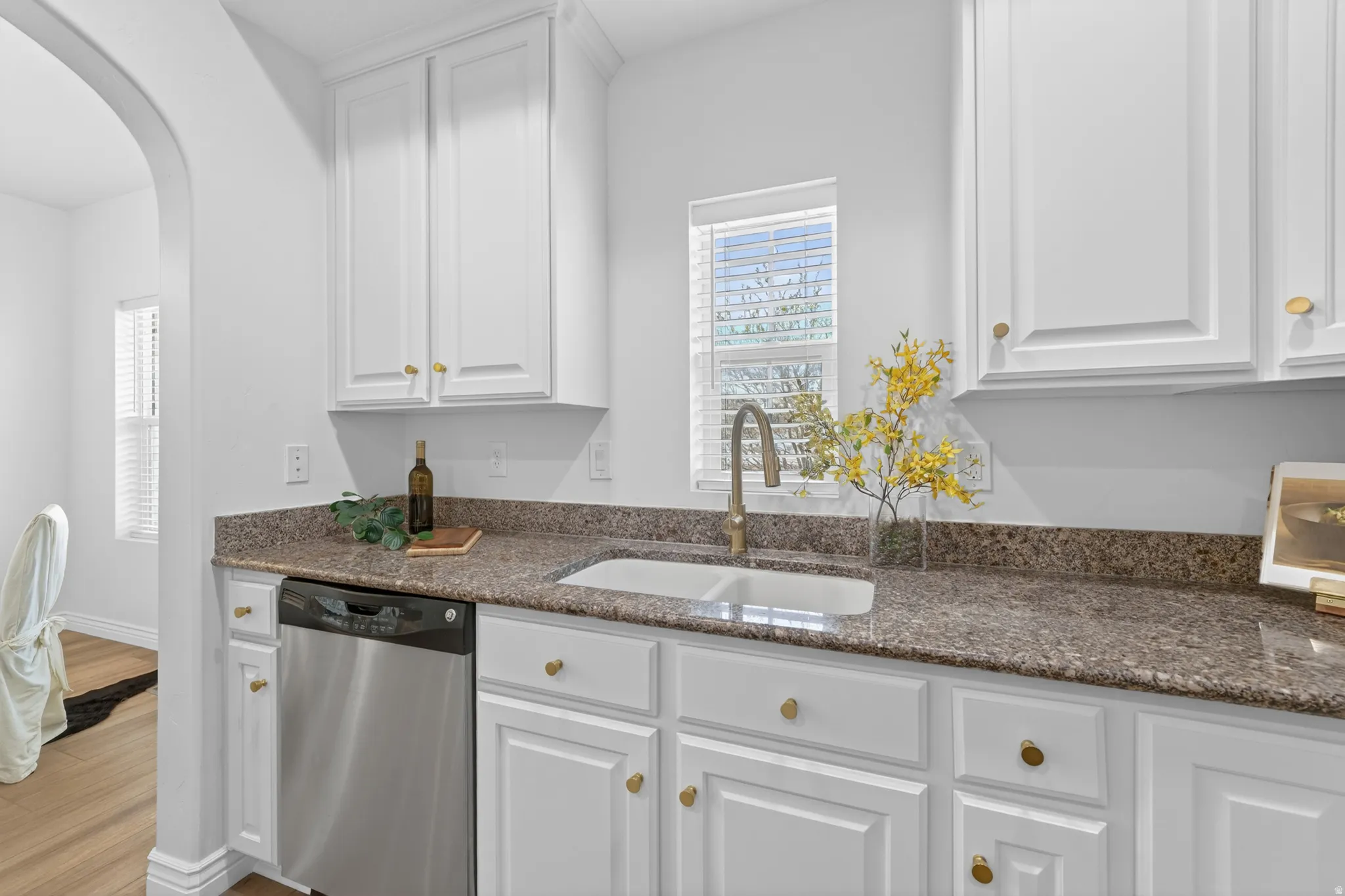 White cabinetry, stainless steel dishwasher, dual-basin sink with a gooseneck faucet, and mottled stone countertops