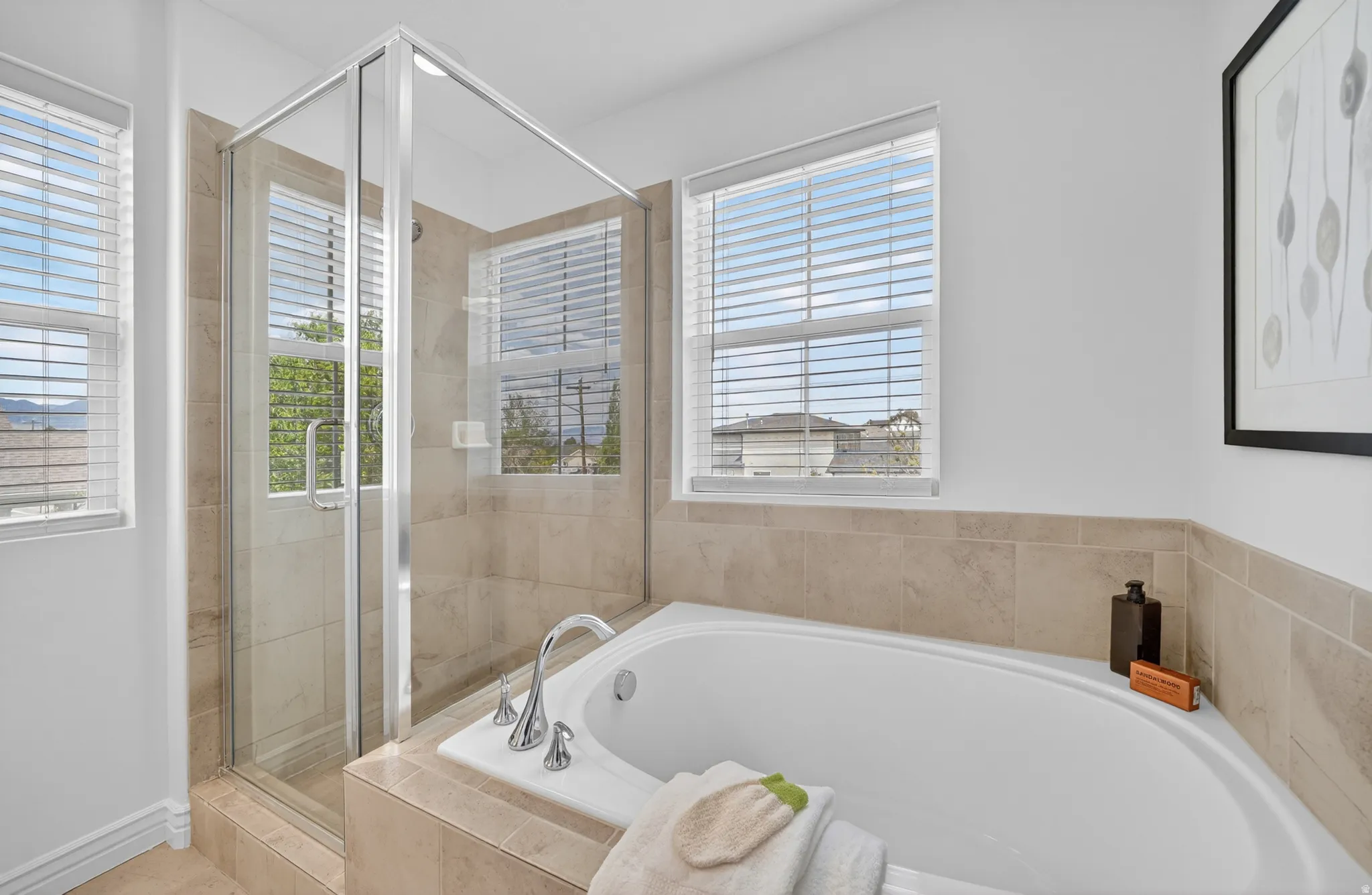 Built-in soaking tub with deck-mounted chrome fixtures, clear glass shower enclosure, and neutral tile surround