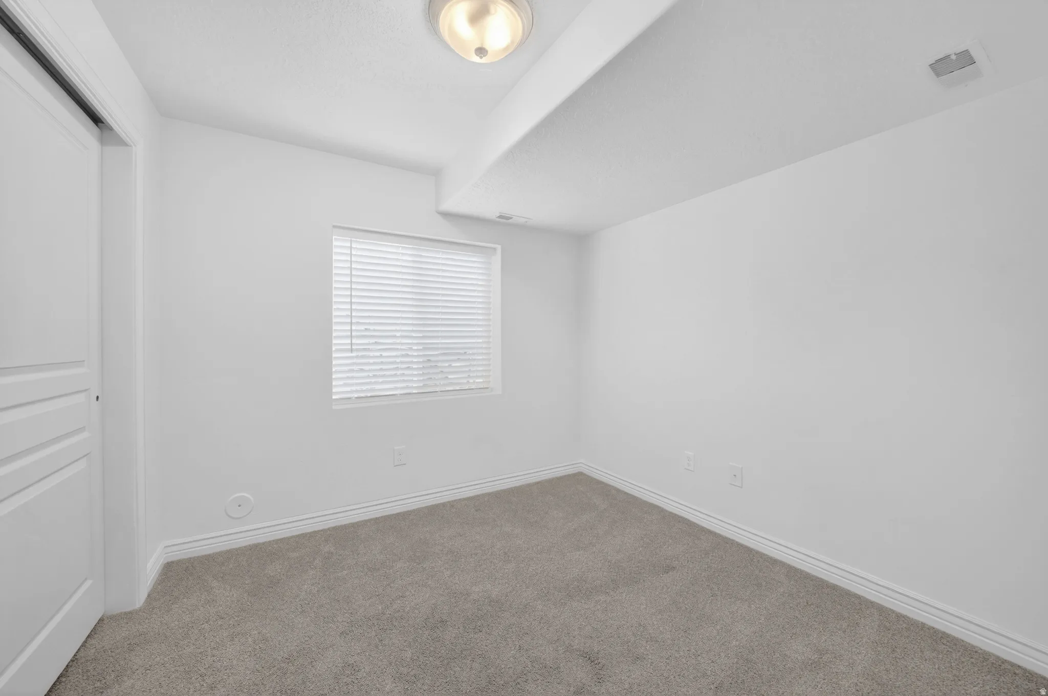 Room featuring light gray carpeting, neutral wall finish, and a window with horizontal blinds