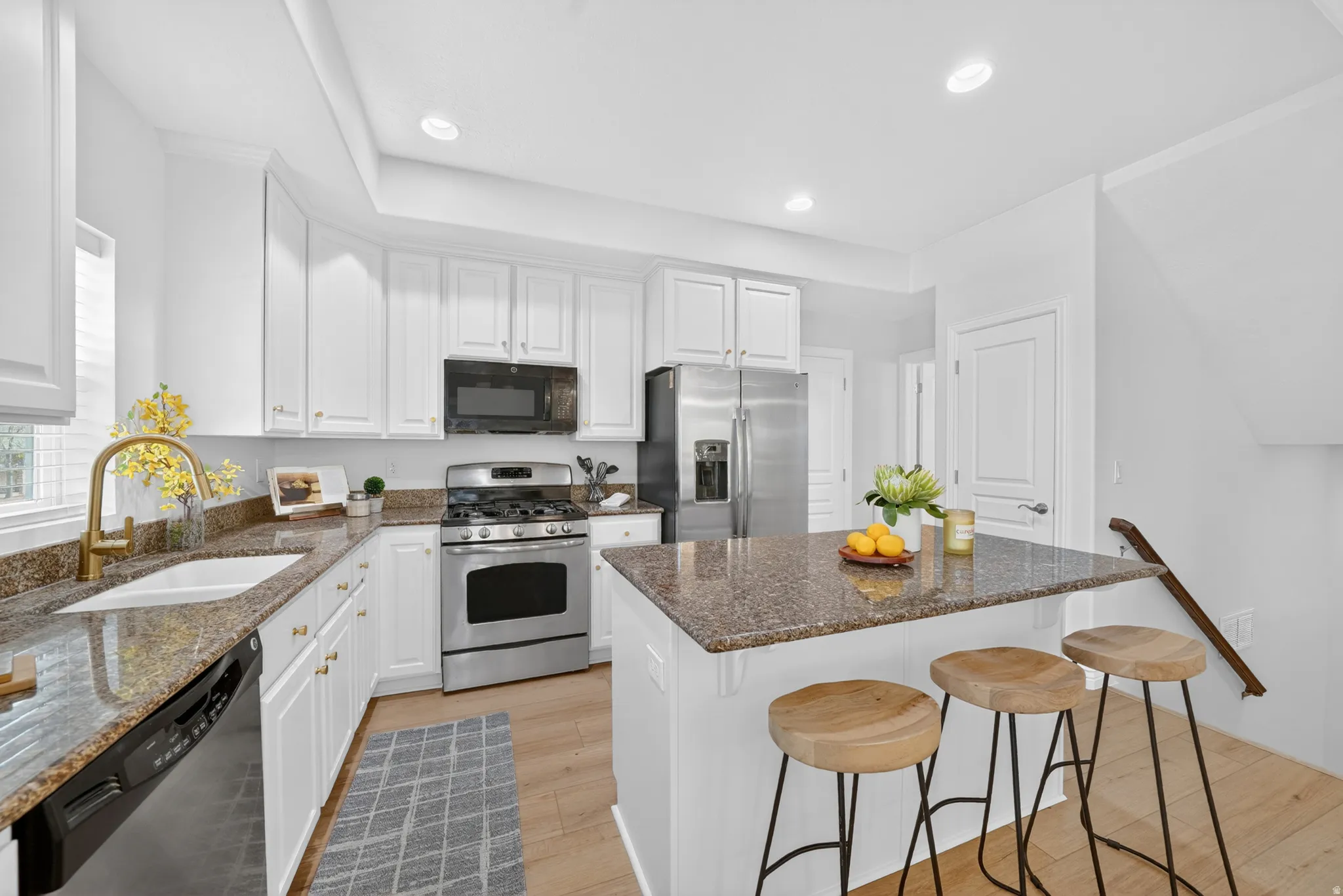Kitchen featuring white cabinetry, granite countertops, stainless steel appliances, a kitchen island with seating, and light wood-finish flooring