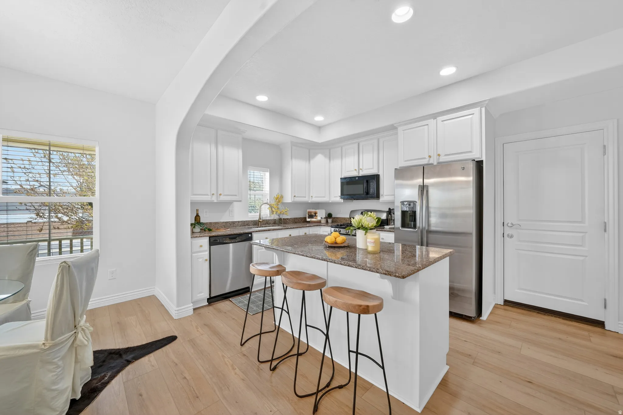 Kitchen featuring an arched entryway, stainless steel appliances, white cabinetry, recessed lighting, and a kitchen island with a stone countertop