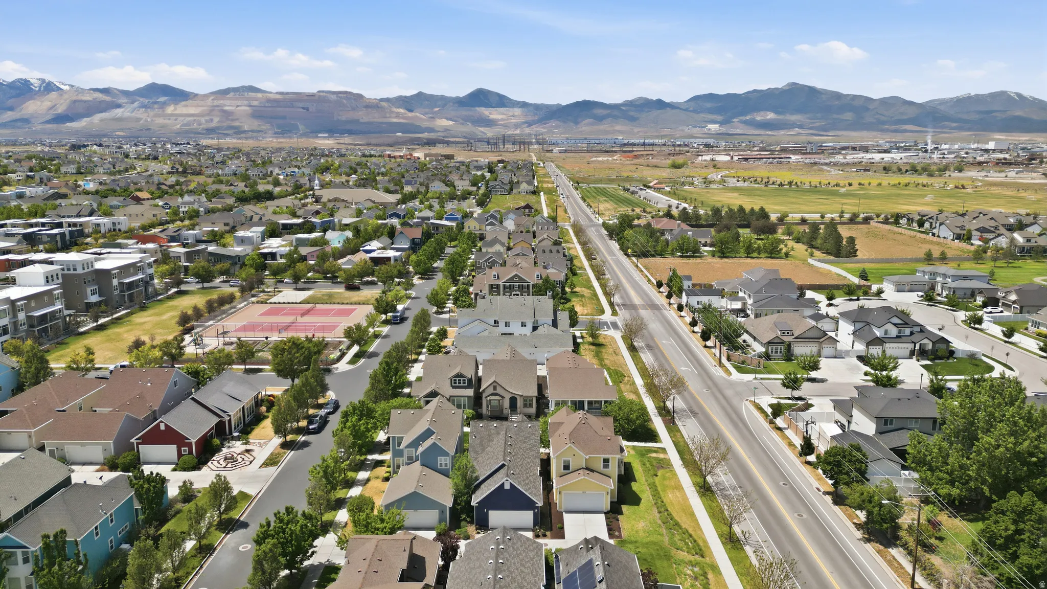 Aerial perspective of a residential neighborhood featuring varied single-family homes, a prominent street, and distant mountain ranges