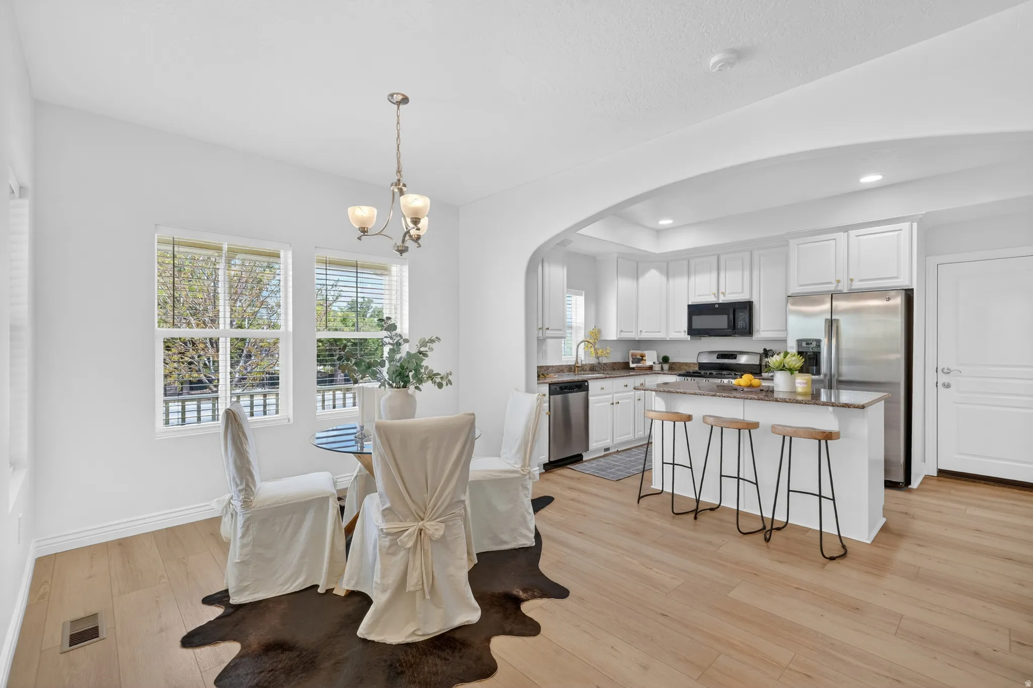 Open-concept living space with wood-finish flooring, recessed lighting, and a kitchen featuring stainless steel appliances, white cabinetry, and a central island with countertop seating