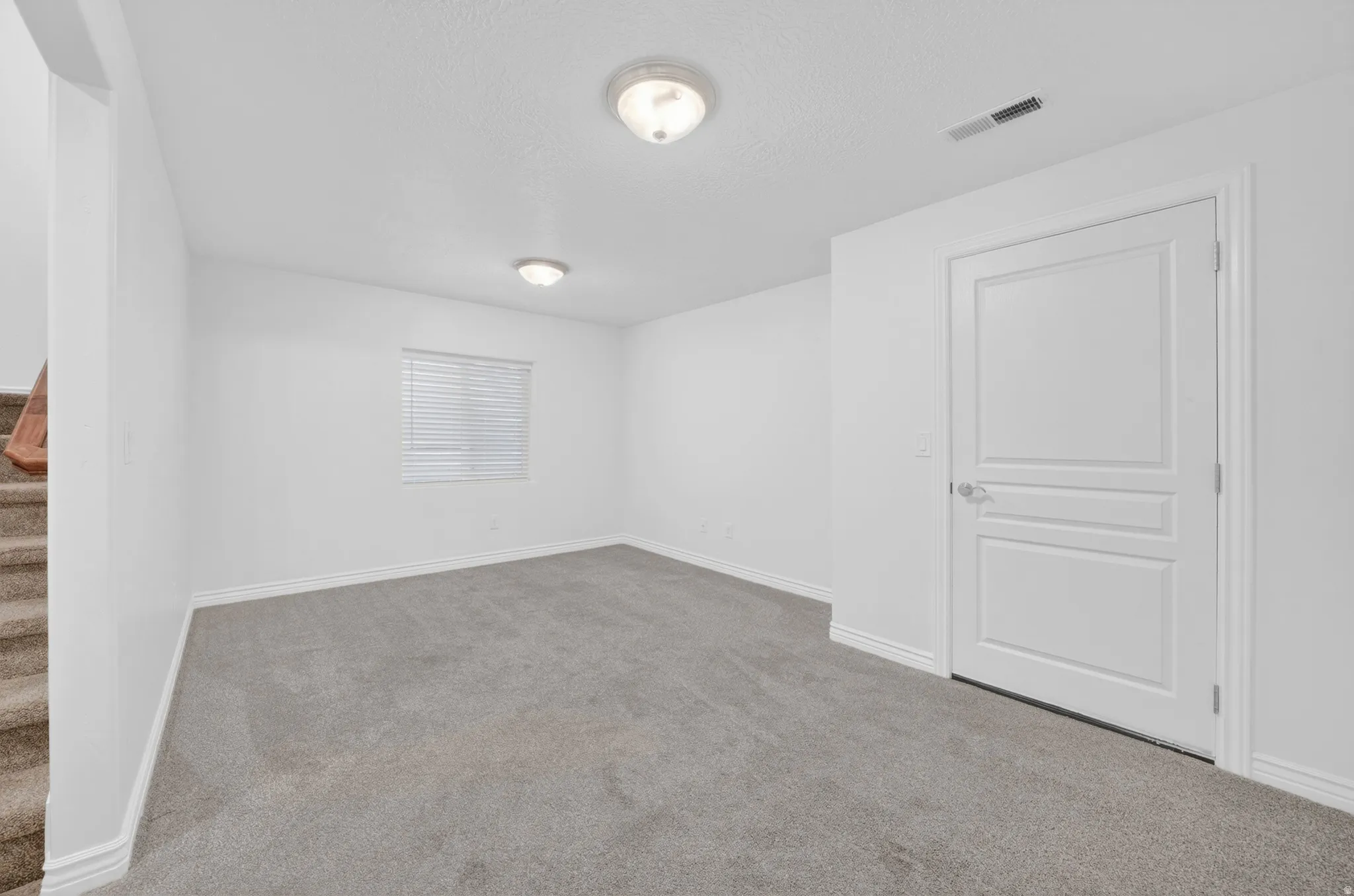 Carpeted room with white walls, window with blinds, panel door, and flush mount ceiling lights