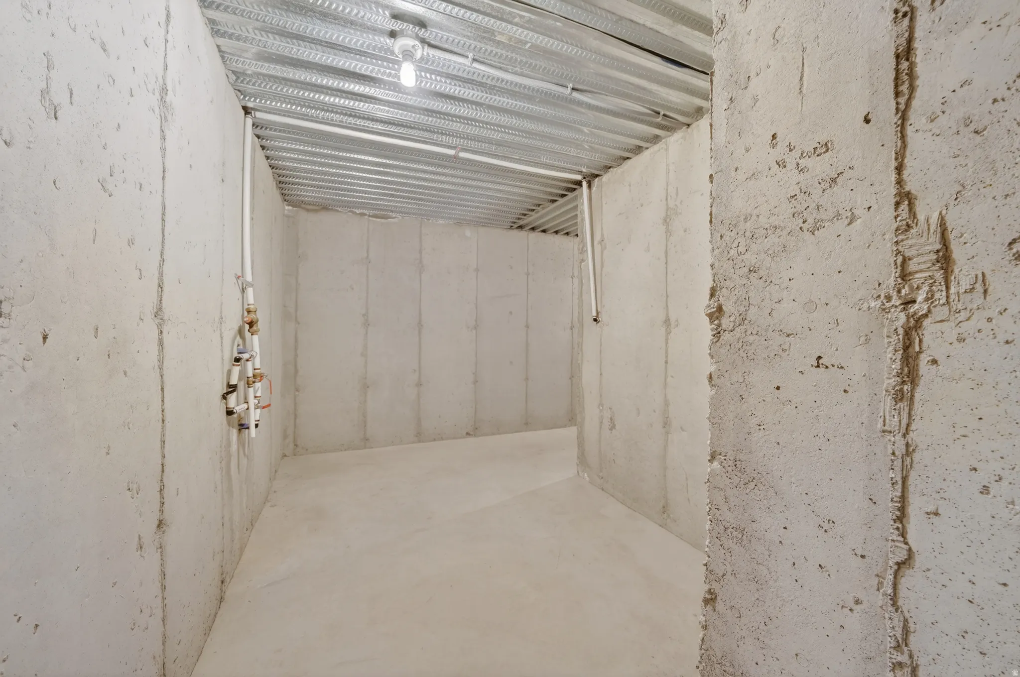 Unfinished space featuring concrete walls and flooring, exposed ceiling joists, and visible plumbing rough-ins