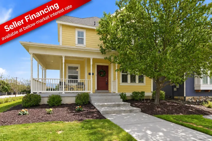 Yellow siding exterior with white trim, covered porch, concrete walkway, red entry door, and manicured landscaping