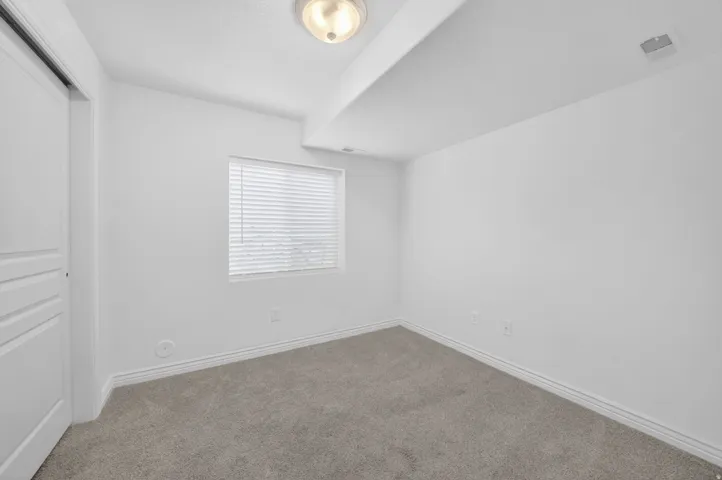 Room featuring light gray carpeting, neutral wall finish, and a window with horizontal blinds