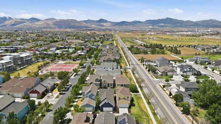 Aerial perspective of a residential neighborhood featuring varied single-family homes, a prominent street, and distant mountain ranges