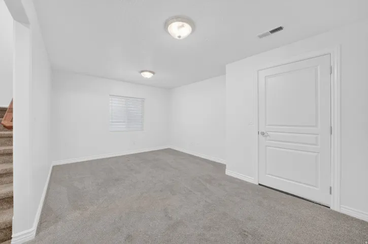 Carpeted room with white walls, window with blinds, panel door, and flush mount ceiling lights