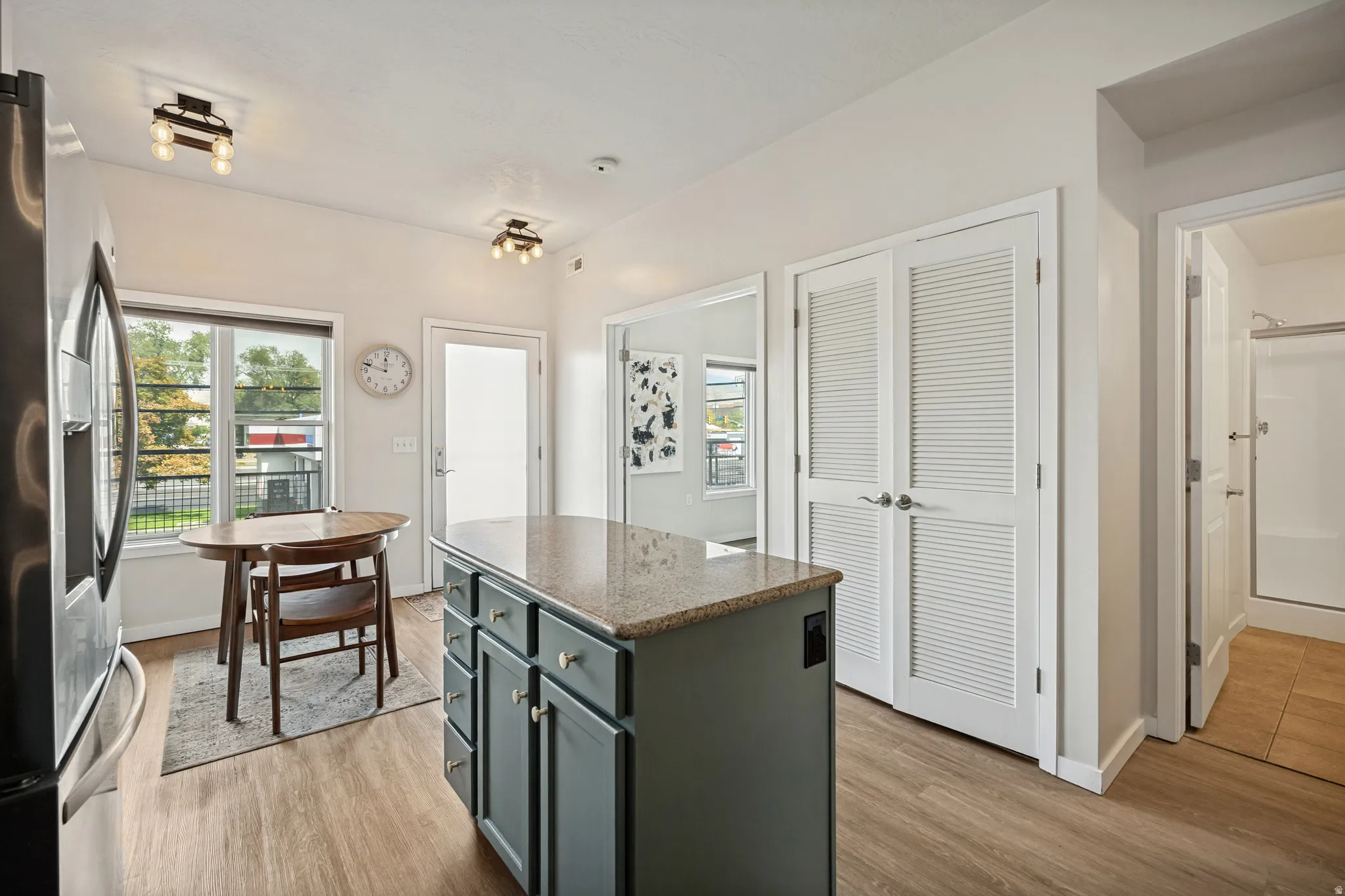 Kitchen area featuring wood-finish flooring, a large window, a kitchen island with a stone-finish countertop, and white louvered bifold doors
