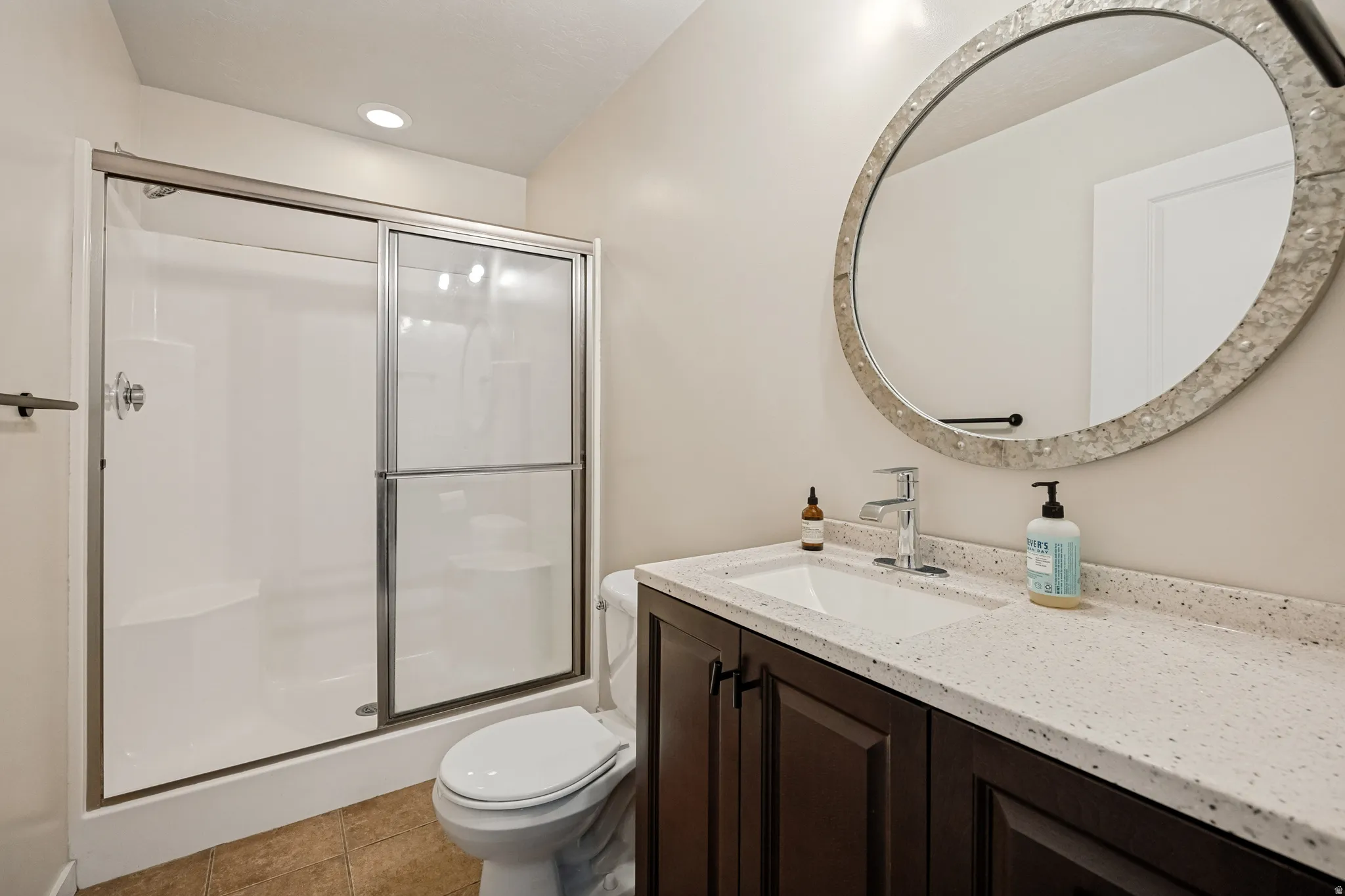 Walk-in shower with sliding glass doors, dark wood-finish vanity with built-in sink, speckled countertop, and large decorative framed mirror