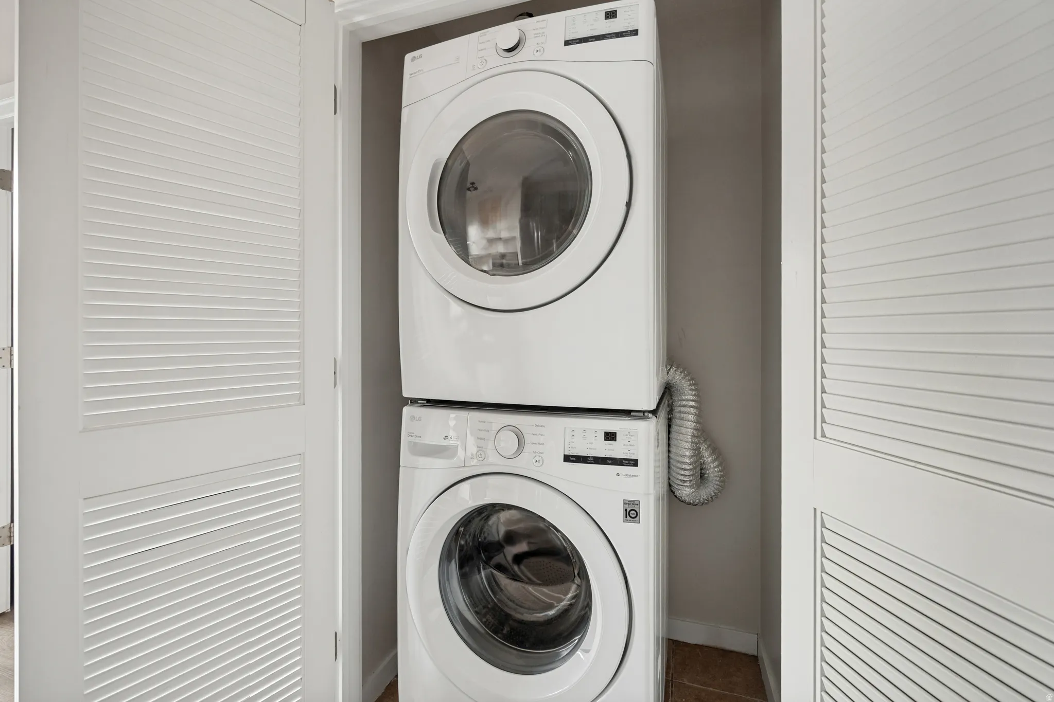 Stacked laundry appliances within a dedicated closet, featuring louvered bi-fold doors