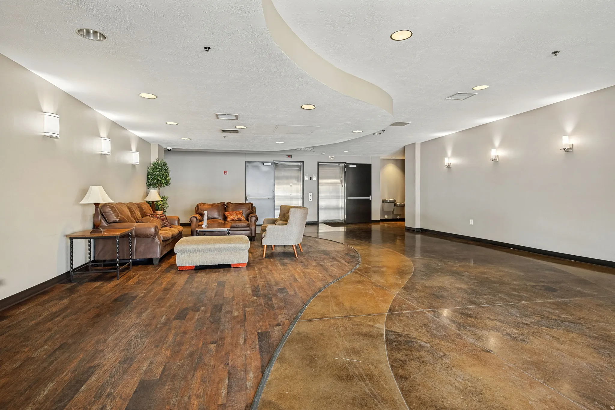 Wood-finish flooring with a decorative concrete inlay, recessed lighting, and wall sconces