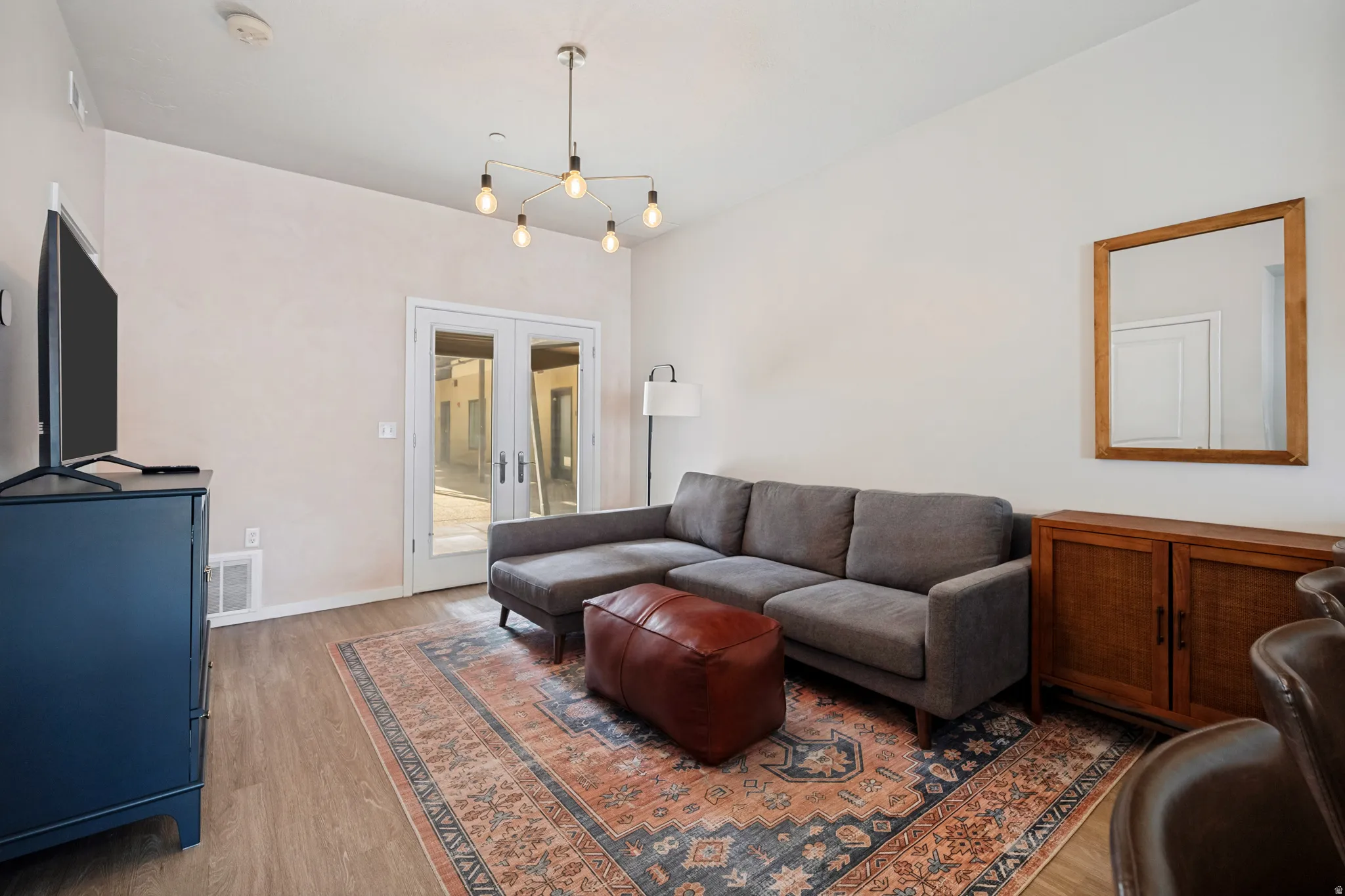 Spacious room featuring high ceilings, wood-finish flooring, a contemporary ceiling light fixture, and French doors