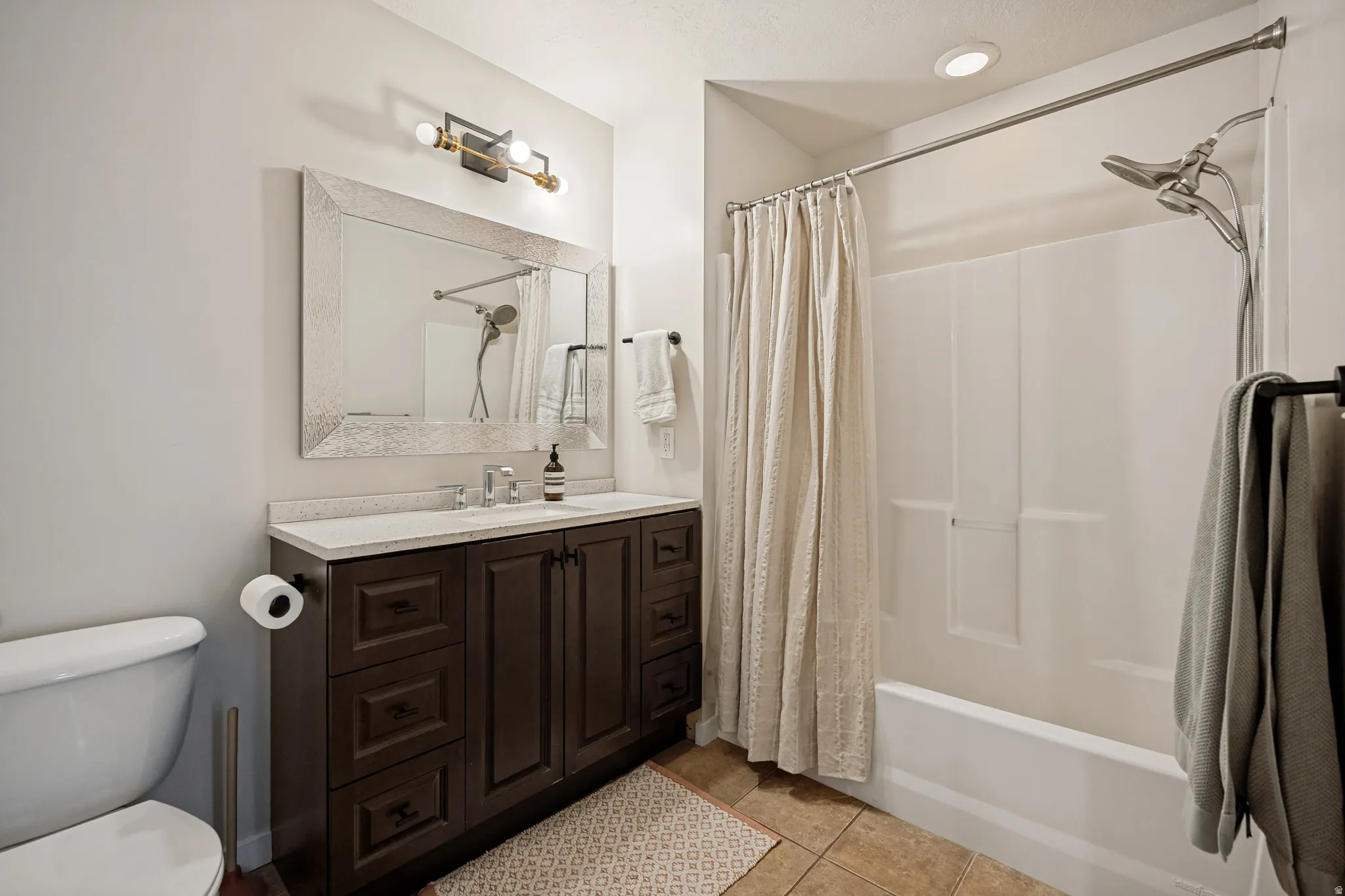 Bathroom featuring a dark wood finish vanity with a light-colored countertop, a framed mirror, a three-light vanity fixture, and a shower-over-tub combination with a wall-mounted showerhead