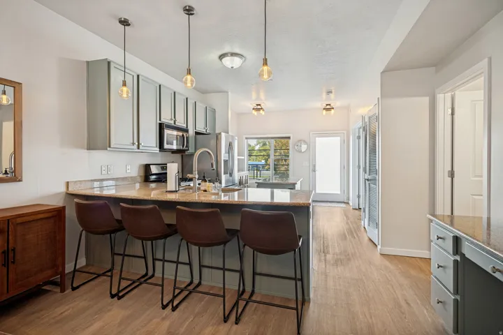 Kitchen featuring wood-finish flooring, light-toned cabinetry, stainless steel appliances, a breakfast bar with stone countertops, and overhead pendant lighting