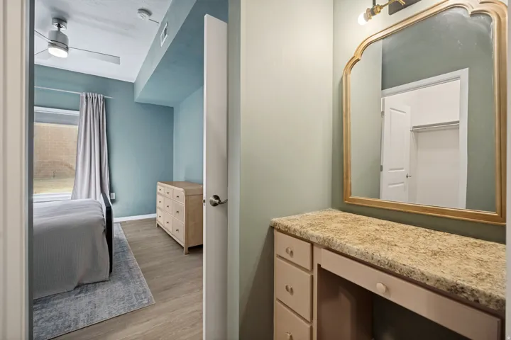 Built-in vanity with a stone-finish countertop, decorative mirror, and wall-mounted lighting