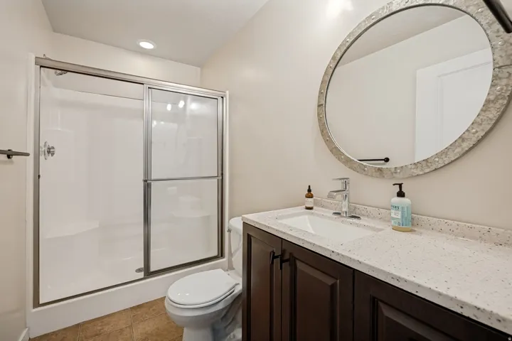 Walk-in shower with sliding glass doors, dark wood-finish vanity with built-in sink, speckled countertop, and large decorative framed mirror