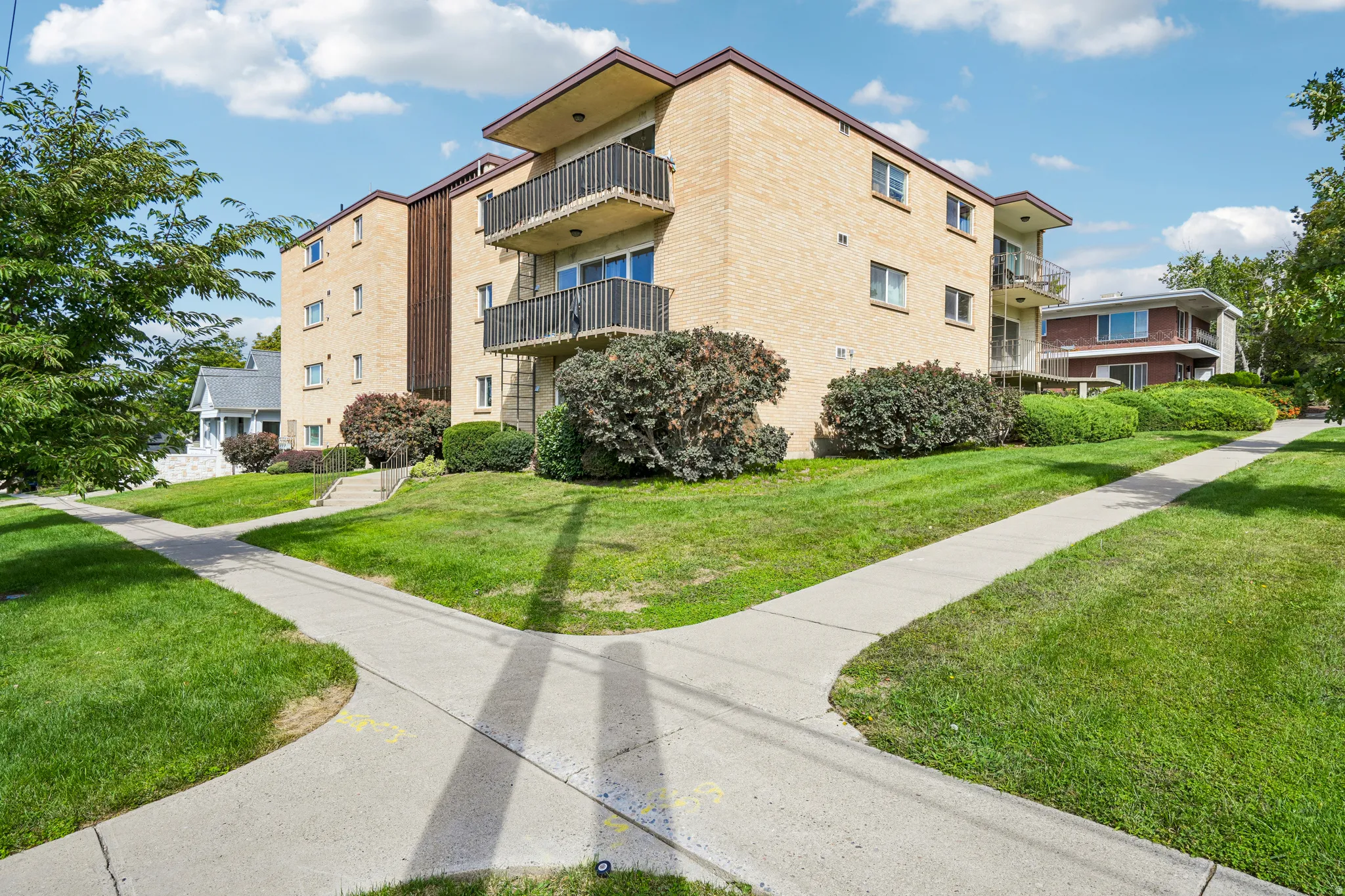 Brick exterior building featuring multiple balconies, established landscaping, and concrete walkways