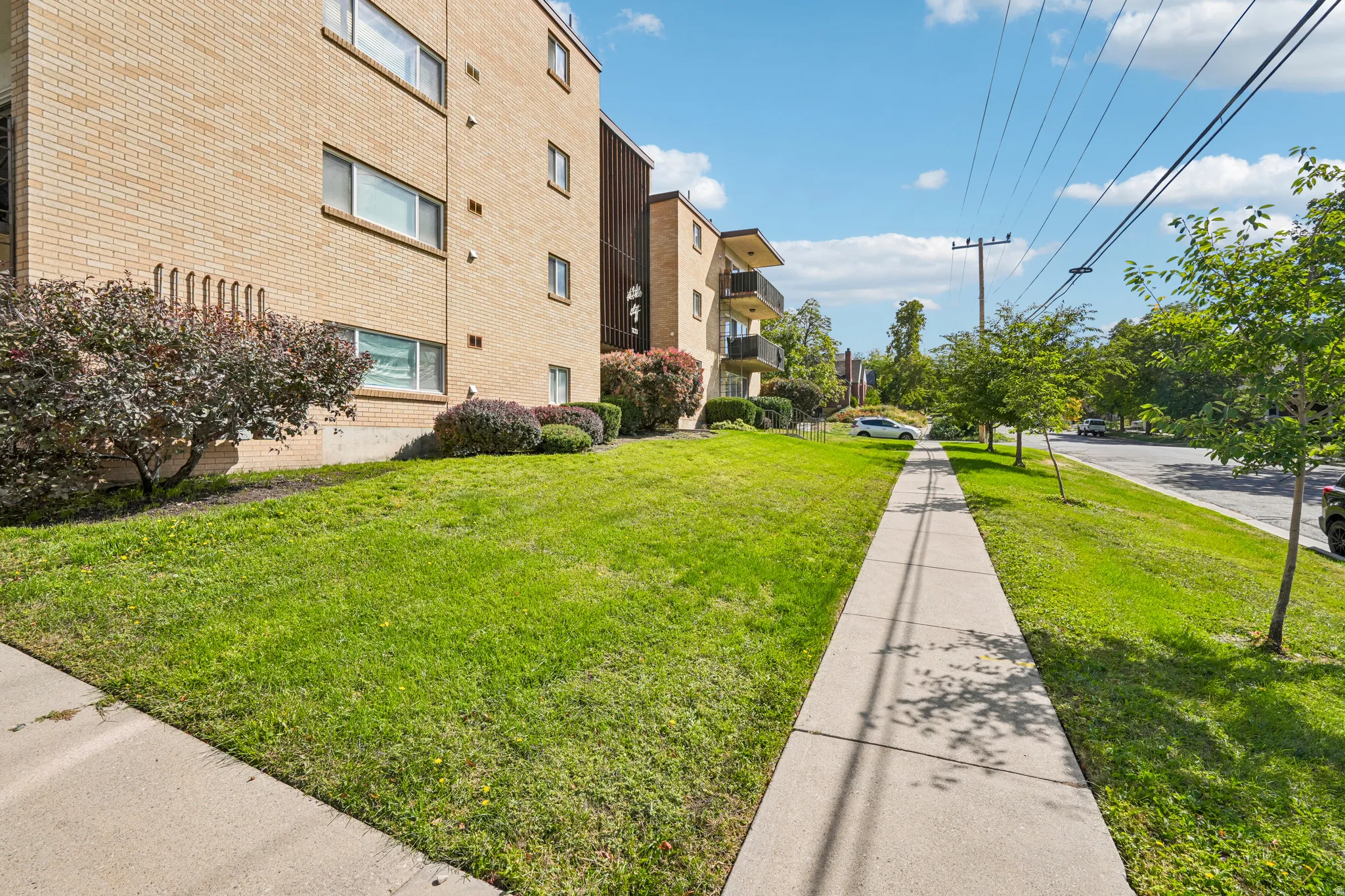 Brick exterior building with multiple windows, balconies with black railings, and surrounding green lawn space
