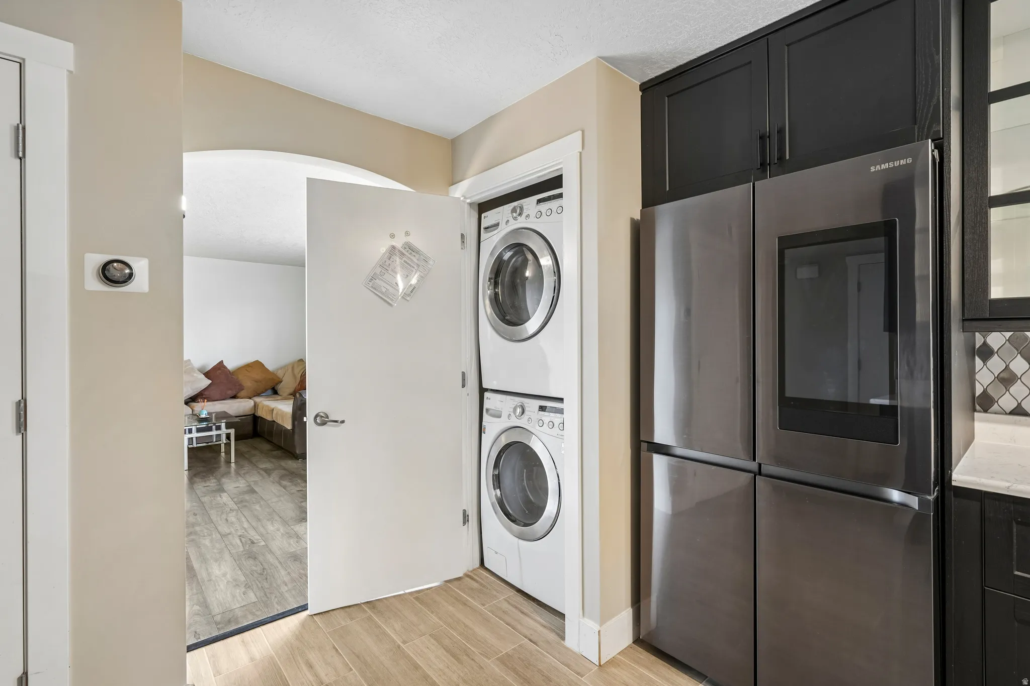 Stainless steel refrigerator with black glass paneling, stackable washer and dryer units, arched doorway, and wood-finish flooring