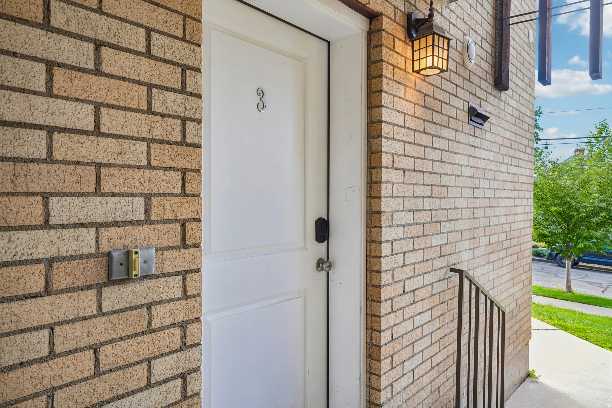 Brick exterior with a white entry door, exterior wall lantern, and metal handrail