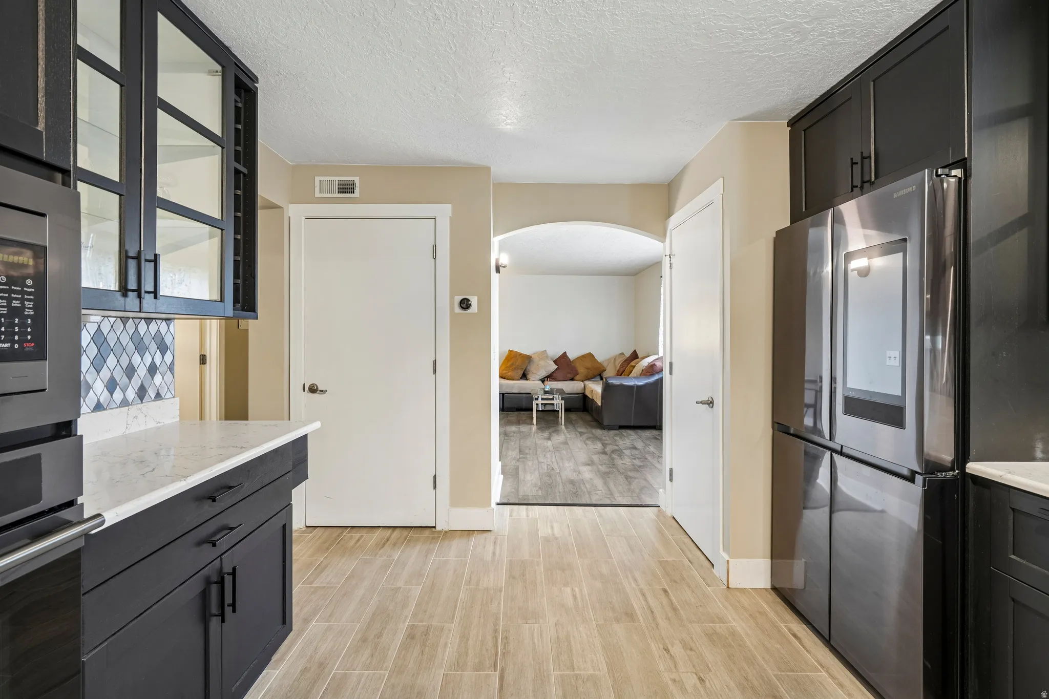 Contemporary black cabinetry, white countertops, a tiled backsplash, wood-finish flooring, and an arched doorway