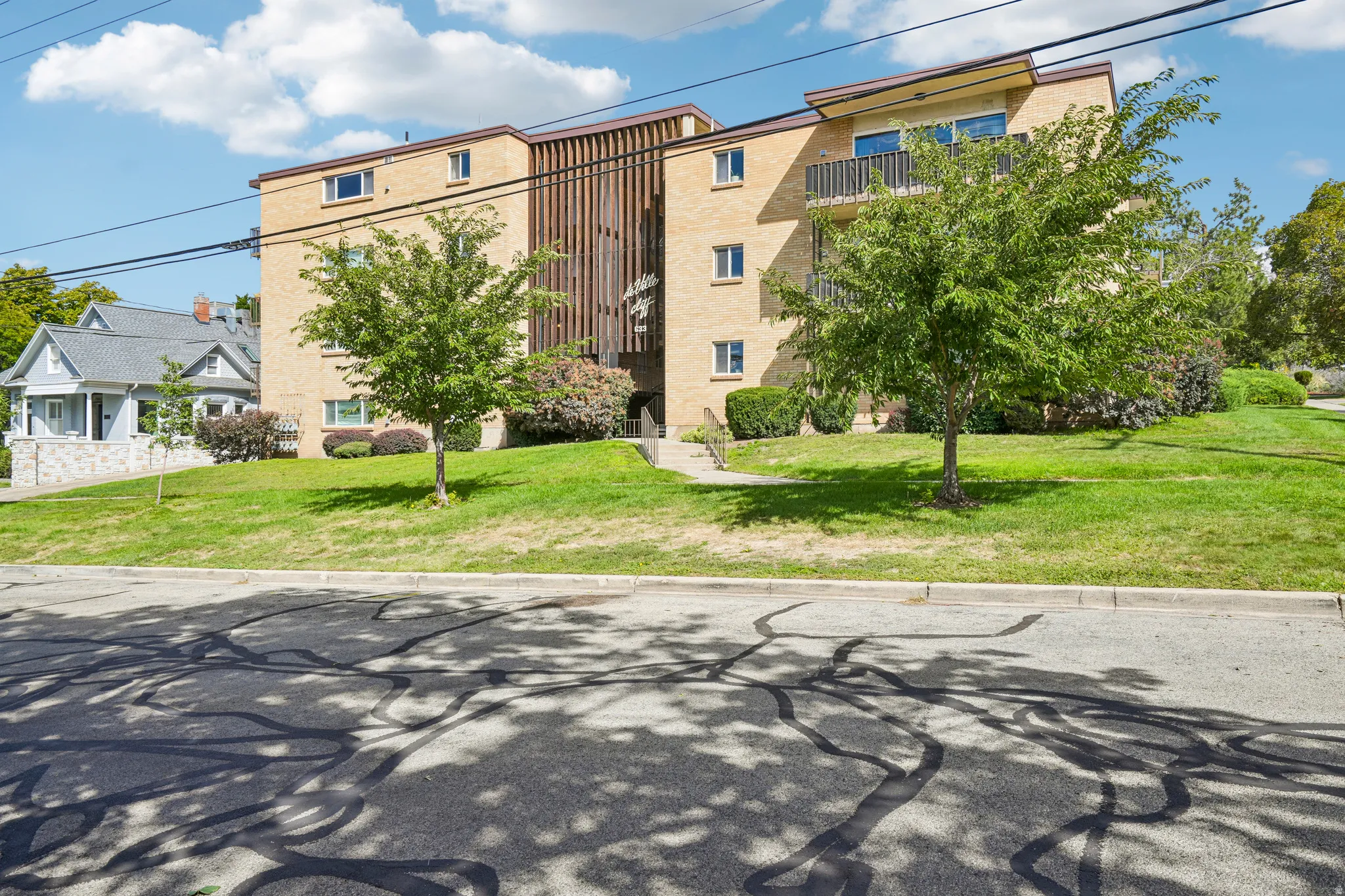 Brick exterior building with multiple balconies, sloped lawn, and mature trees