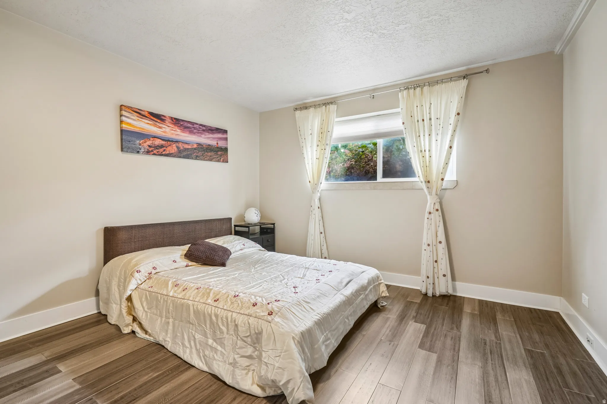 Wood-finish flooring, neutral wall tones, window with natural light, white trim, and a textured headboard