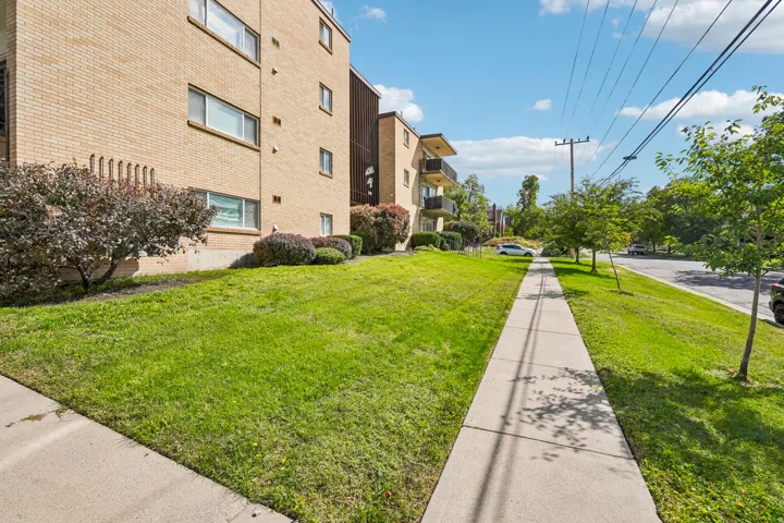 Brick exterior building with multiple windows, balconies with black railings, and surrounding green lawn space