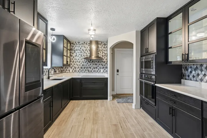 Stainless steel appliances, light-toned wood-finish flooring, dark cabinetry, mosaic tile backsplash, and light countertops