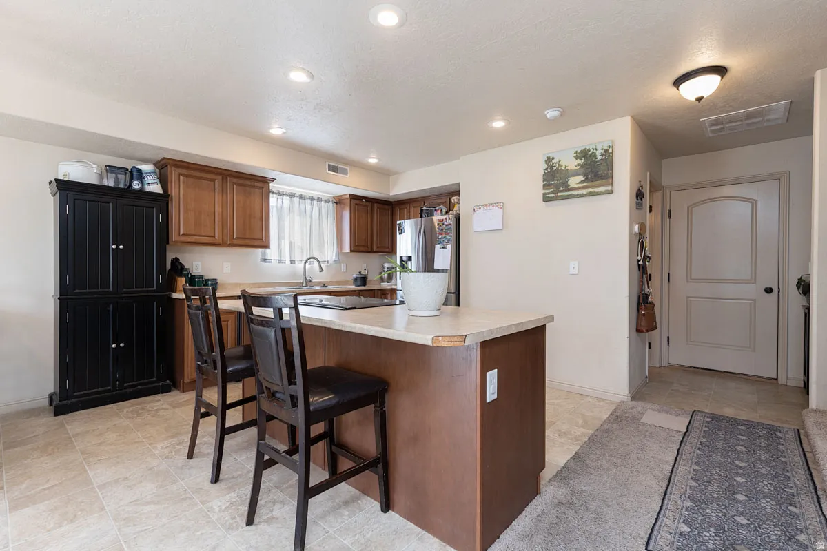Kitchen featuring wood-finish cabinetry, a central island with bar seating, recessed lighting, and tile flooring
