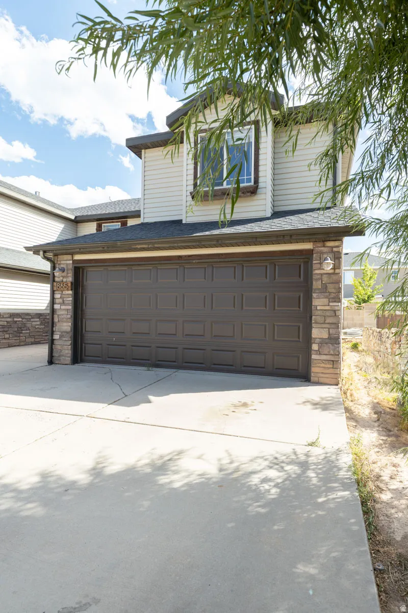 Attached two-car garage with a panel door, stone façade accents, and a concrete driveway