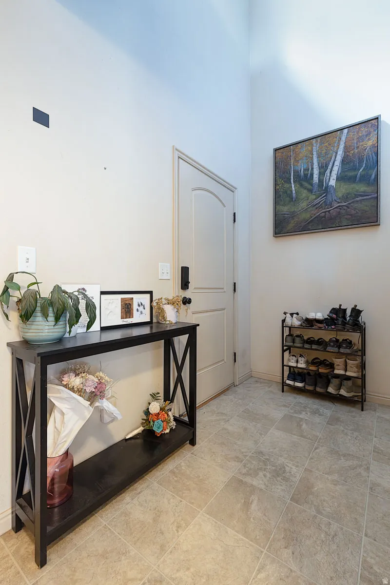 Vaulted ceiling, arched interior door, modern door hardware, wall-mounted light switch, and square tile flooring