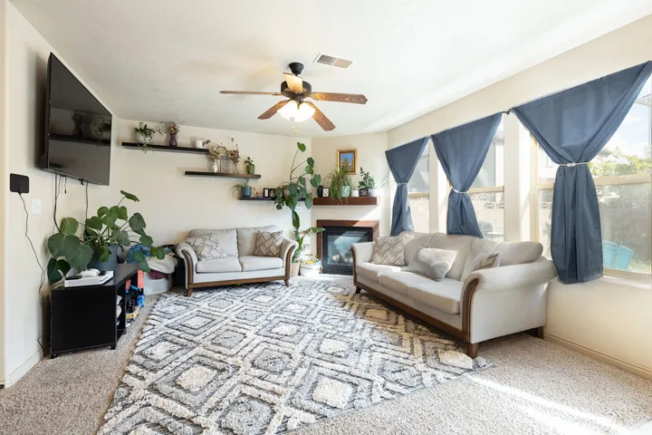 Recessed fireplace with wood mantel, multiple windows, ceiling fan, and wall-mounted shelving