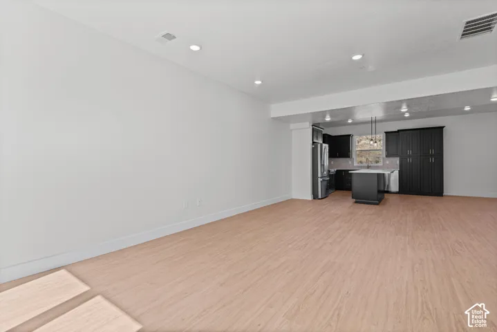 Open-concept living area featuring wood-finish flooring, recessed lighting, and a kitchen with dark cabinetry, stainless steel appliances, and a central island with a sink