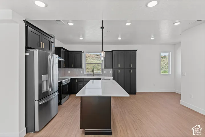 Modern kitchen featuring dark cabinetry, stainless steel appliances, a center island with a light-colored countertop, and recessed lighting
