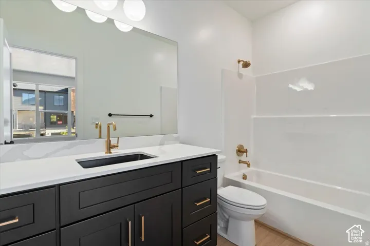 Modern bathroom featuring a dark wood-finish vanity with gold-tone hardware, white countertop, and integrated white tub-shower combination