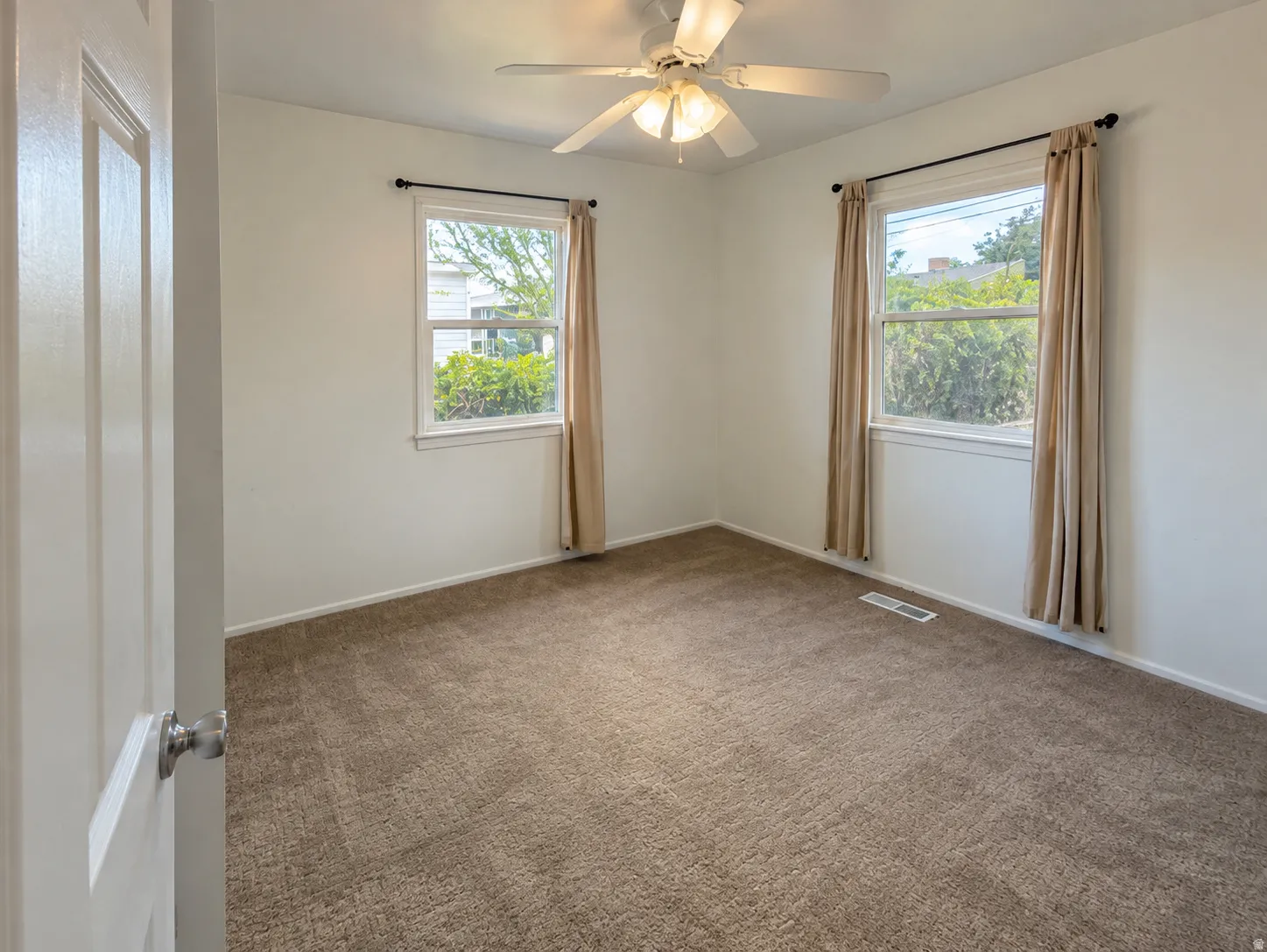 Neutral wall finishes, textured carpet flooring, two windows with trim, and a ceiling fan with integrated lighting