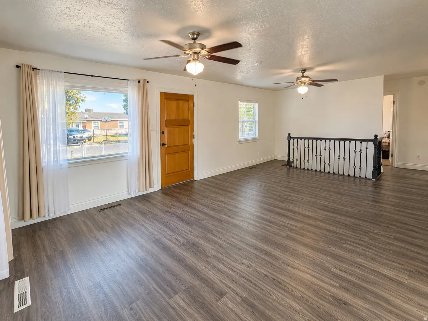 Wood-finish flooring throughout, bright white walls, multiple ceiling fans with integrated lighting, and a dark-toned iron railing