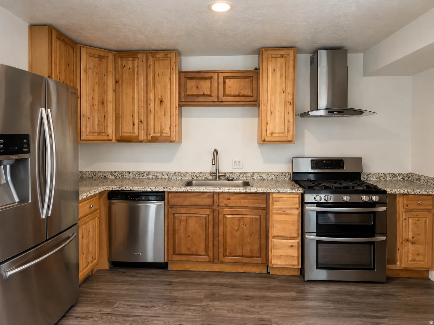 Kitchen featuring wood-finish cabinetry, light-toned countertops, stainless steel appliances, and wood-finish flooring