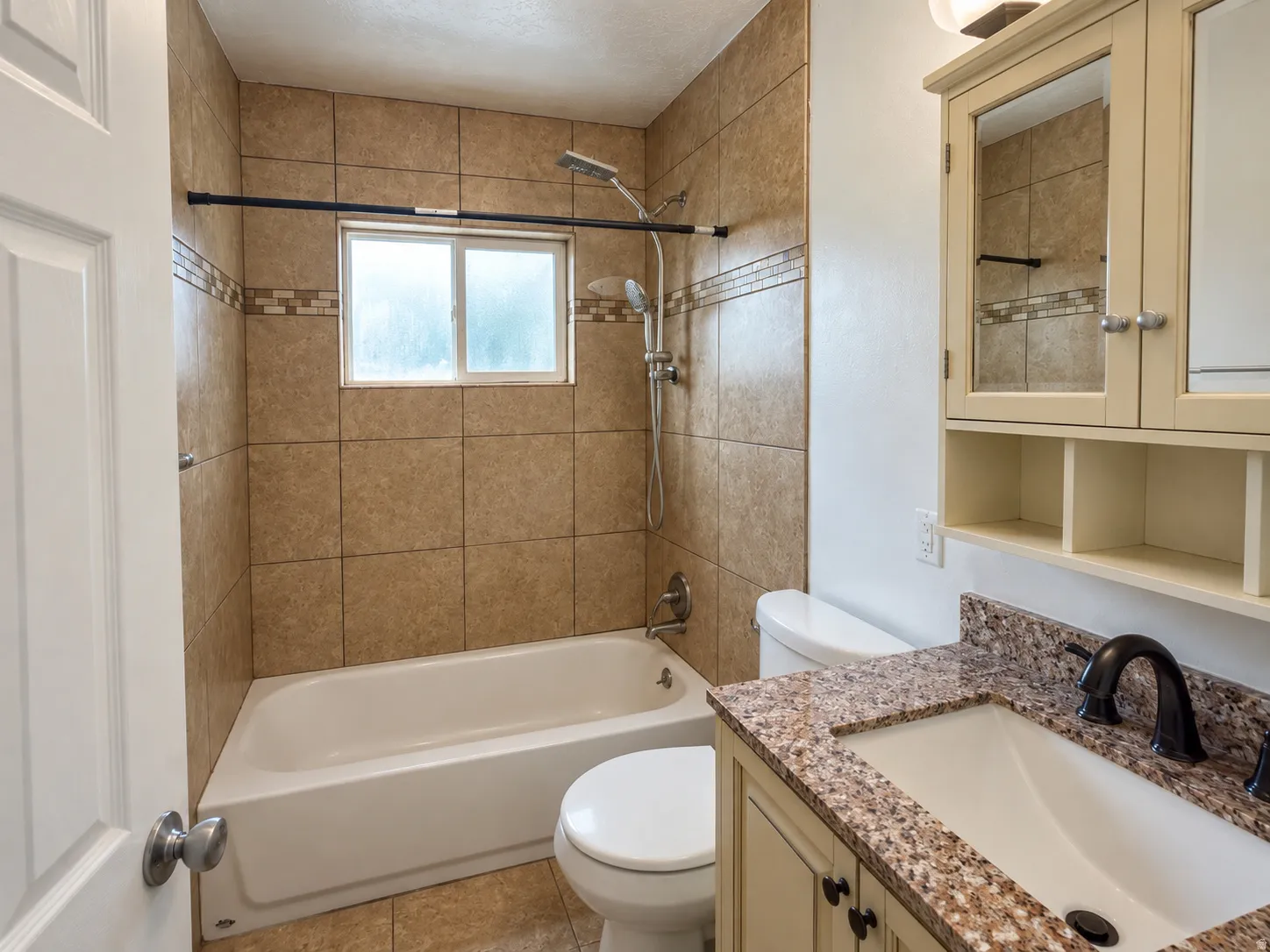 Tiled shower surround with decorative accent band, white bathtub, vanity with granite-style countertop, integrated sink, and dark bronze-finish faucet