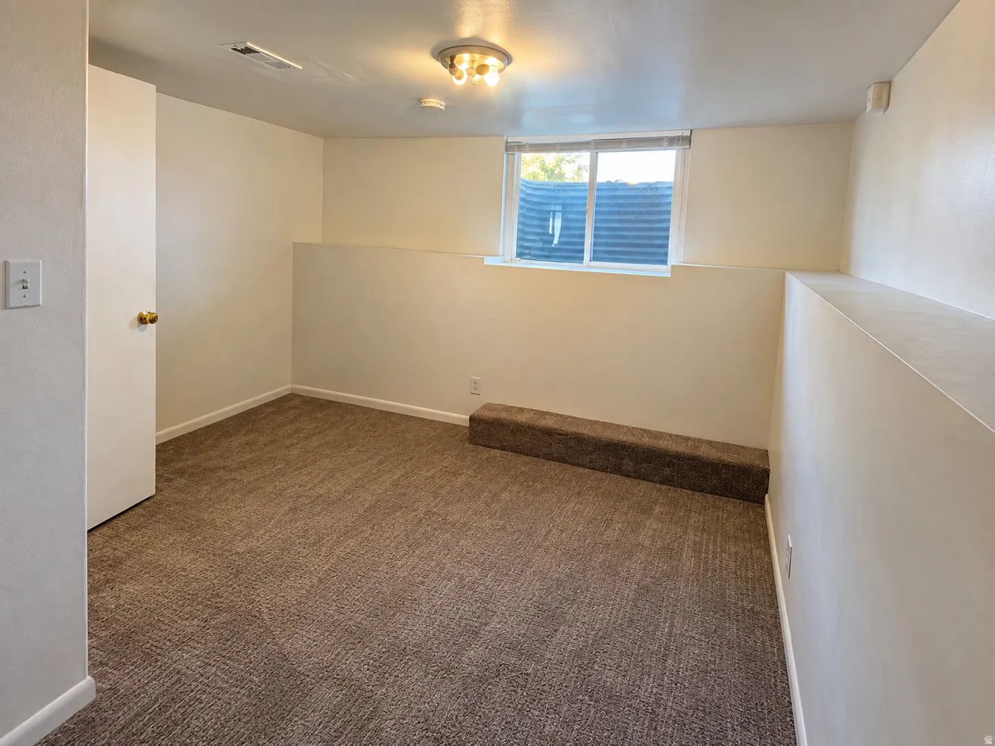 Recessed window with white trim, wall-mounted light fixture, carpeted flooring, and a neutral color palette