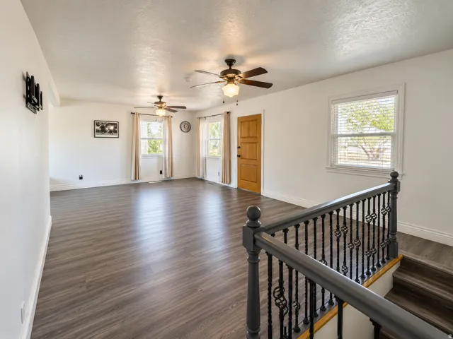 Spacious living area featuring wood-finish flooring, multiple windows, and two ceiling fans with integrated lighting