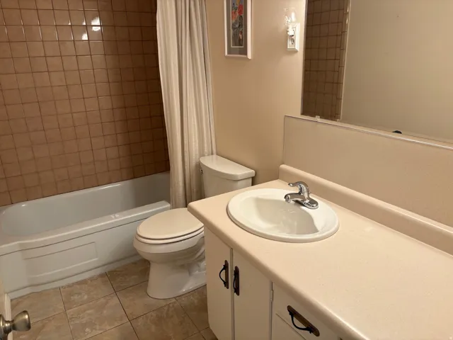 Built-in bathtub with subway tile surround, ceramic tile flooring, single vanity with integrated sink, and wall-mounted light fixture